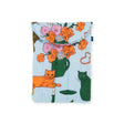 The Baggu Puffy Laptop Sleeve 13"/14" - Table Cats by Baggu boasts a charming quilted pouch crafted from recycled materials and features a delightful Table Cats print, enhanced with floral designs in vibrant orange, green, and purple shades on a light blue background.