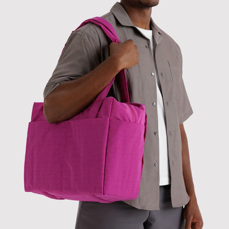 Bright magenta fabric tote bag with wide handles and spacious exterior pockets carried on shoulder by person in casual shirt