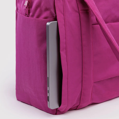 Deep pink fabric backpack side pocket holding a silver laptop on a light background