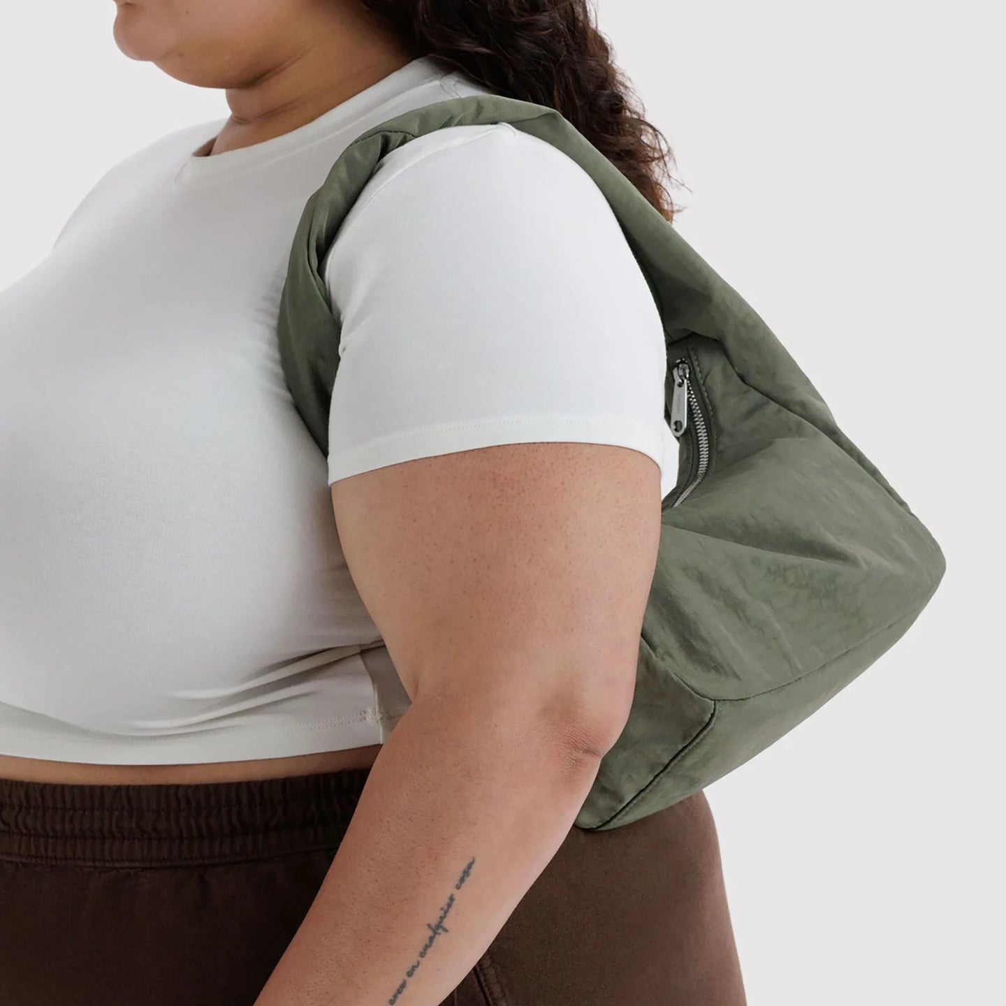Small olive-green nylon hobo bag worn on the shoulder over a white shirt