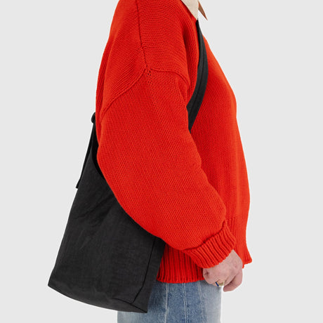 A person wearing a red sweater and jeans carries a stylish black Baggu Small Nylon Sling - Black from the brand Baggu.