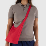 A person wearing a gray polo shirt and navy pants carries a Candy Apple Baggu Small Nylon Sling.