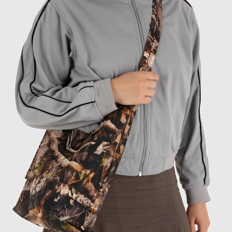 A person wearing a gray jacket and brown skirt carries a Baggu Small Nylon Sling - Photo Forest over their shoulder.