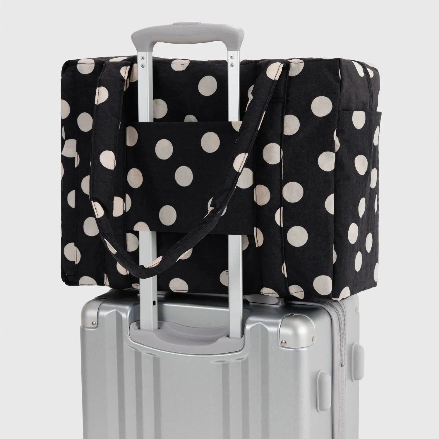 Polka-dot tote bag with cream dots, secured over a carry-on suitcase
