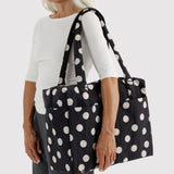 Black tote bag with cream polka dots, long handles, worn over shoulder