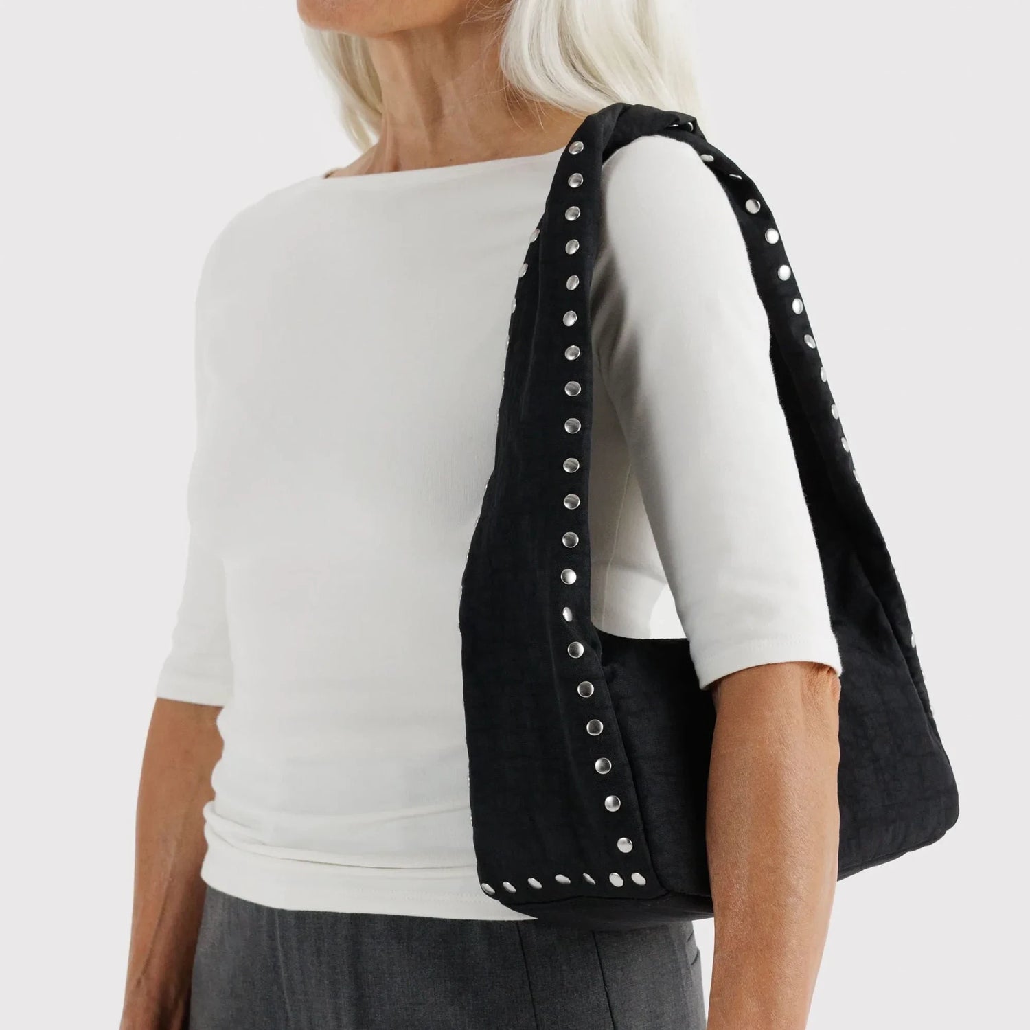 Black nylon hobo bag with studded straps, carried by woman