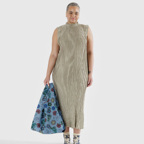 A person in a pleated beige dress holds a Baggu Standard Reusable Bag - Digital Denim Birds, crafted by the brand Baggu. The scene is set against a white background.