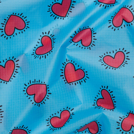 The Baggu Standard Bag - Keith Haring Hearts by Baggu features a vibrant design on blue fabric, adorned with multicolored hearts outlined by black dashes, inspired by Keith Haring's iconic style. Crafted from recycled nylon, this bag is both eco-friendly and artistically dynamic.