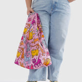 A person holds a tote bag from the Baggu collection, featuring a vibrant cartoon cat pattern and crafted from recycled nylon.