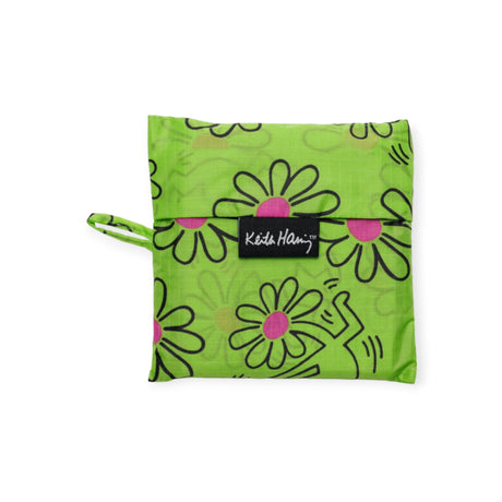 A green pouch made from recycled nylon yarn, with a floral and abstract pattern, is decorated with a black label featuring white text. It is the Baggu Standard Bag - Keith Haring Flower by Baggu.