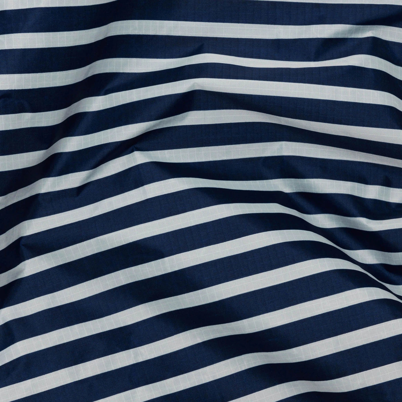 The Baggu Standard Reusable Bag in Navy Stripe showcases a slightly wrinkled texture, echoing the classic navy stripe design.