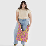 A person holding the Baggu Standard Reusable Bag in Rose, embodying eco-conscious fashion, wears a beige top and jeans while standing against a plain background.