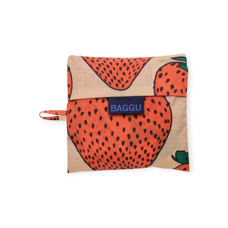 The Baggu Standard Reusable Bag in the Strawberry design is made from sustainable nylon, folds neatly into a square pouch, and features a playful strawberry print along with the iconic "BAGGU" label.