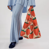 A person dressed in blue clothing holds a Baggu Standard Reusable Bag - Strawberry by Baggu, crafted from sustainable beige nylon and featuring an enchanting strawberry design.