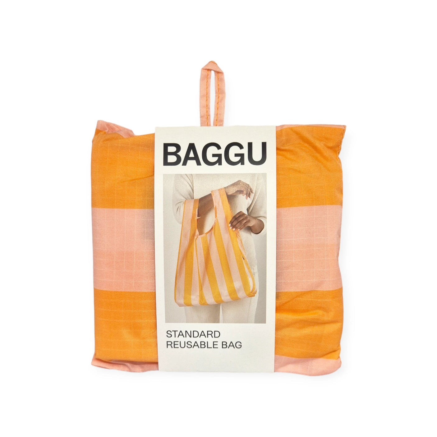 Folded Baggu Standard Reusable Bag - Tangerine Stripe in packaging, featuring a label with an image of a person holding the recycled nylon bag, in orange and pink tangerine stripes.