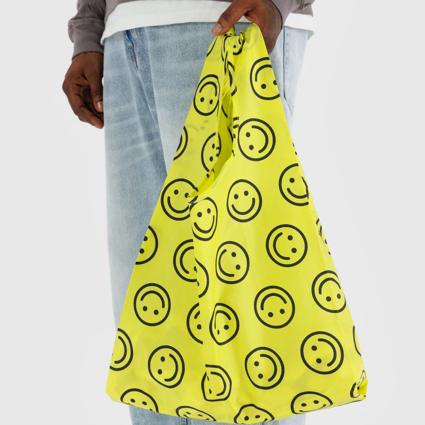 A person holding a Baggu Standard Reusable Bag - Yellow Happy by Baggu, featuring black smiley faces.