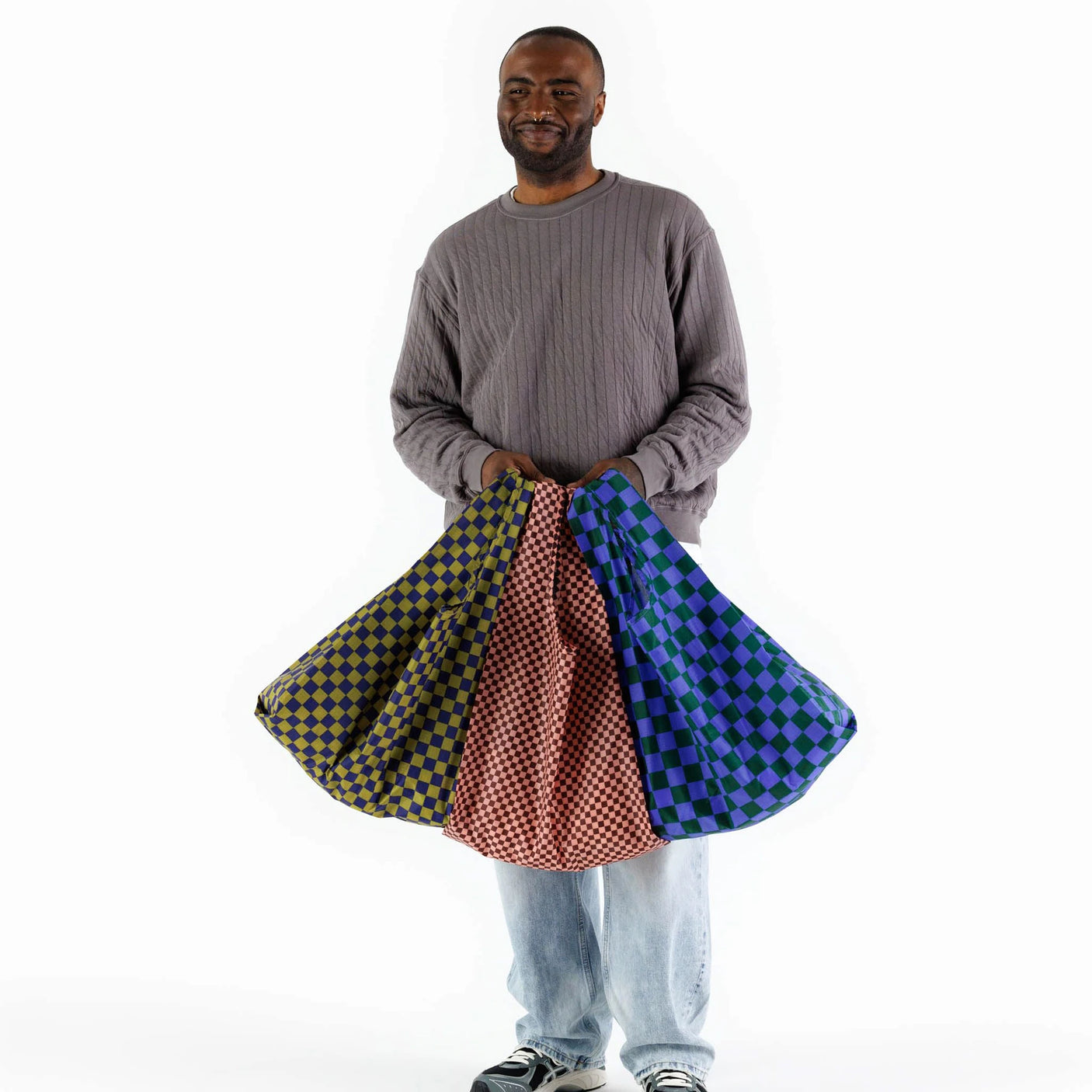 A man holds up three checkered fabrics in vibrant jewel tones—yellow, red, and blue—that remind one of the colorful patterns featured in the "Baggu Set of 3 Standard Bags - Jewel Checks" by Baggu.