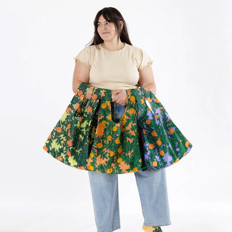 A person in a beige t-shirt and jeans holds a vibrant Baggu set of 3 standard bags featuring orange tree patterns, made from eco-friendly materials.