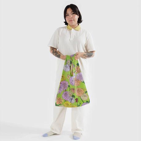 A person in a white outfit holds a Baggu Standard Reusable Bag - Dahlia against a plain white background, highlighting an eco-friendly choice by the brand Baggu.