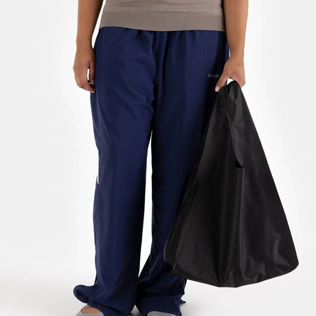 A person is wearing a beige top and blue pants while holding the Baggu Standard Reusable Bag in black, standing against a plain background.