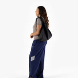 A person in a gray shirt and blue pants is holding a black Baggu Standard Reusable Bag while standing against a plain white background.