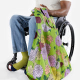 A person in a wheelchair holds the Big Baggu Bag - Dahlia from Baggu, featuring a vibrant dahlia print and expertly crafted from recycled nylon.