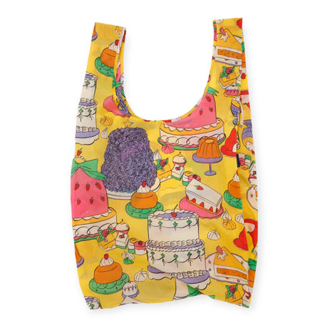 The Big Baggu Bag - Patisserie from Baggu is an eco-friendly reusable bag adorned with a charming print of cakes, pudding, and macarons against a vibrant yellow background.