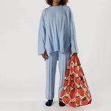 A person in a light blue outfit holds the oversized Baggu Big Baggu Bag - Strawberry, featuring a red strawberry pattern.