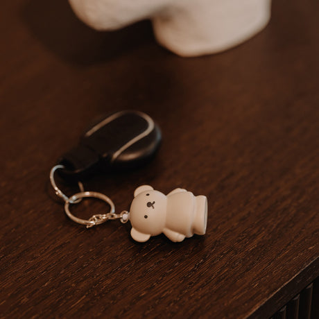 Cream-colored bear-shaped keychain with simple facial features attached to black retractable badge holder on wooden surface