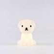 The Snuffy Dog Miffy Night Light (15cm) by Miffy, made from BPA-free silicone, softly glows against a simple gray backdrop. Its delightful design, inspired by Miffy and Friends, showcases black accents that animate this small white dog-shaped lamp.