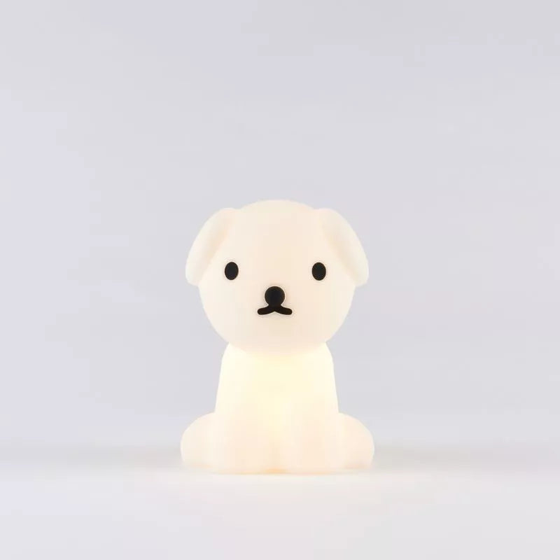 The Snuffy Dog Miffy Night Light (15cm) by Miffy, made from BPA-free silicone, softly glows against a simple gray backdrop. Its delightful design, inspired by Miffy and Friends, showcases black accents that animate this small white dog-shaped lamp.