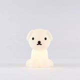 The Snuffy Dog Miffy Night Light (15cm) by Miffy, made from BPA-free silicone, softly glows against a simple gray backdrop. Its delightful design, inspired by Miffy and Friends, showcases black accents that animate this small white dog-shaped lamp.