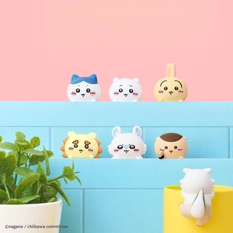 Six small, round Sonny Angel figures from the Chiikawa Hippers Blind Box are displayed on blue shelves. In the foreground, a potted plant and another Chiikawa Hippers Blind Box figurine in a yellow cup stand out against a pink background.