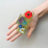 Transparent claw clip holding colorful daisies on clear green-tinted backing