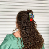 Flower claw clip on long dark curly hair with small colorful flower accents