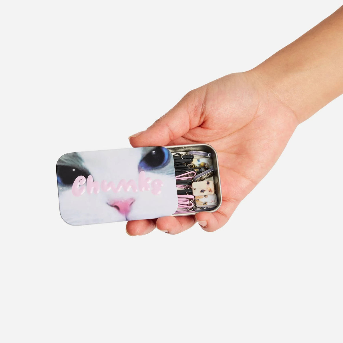 Cat-themed bobby pin tin held in hand, showing mixed pins with pink striped accents