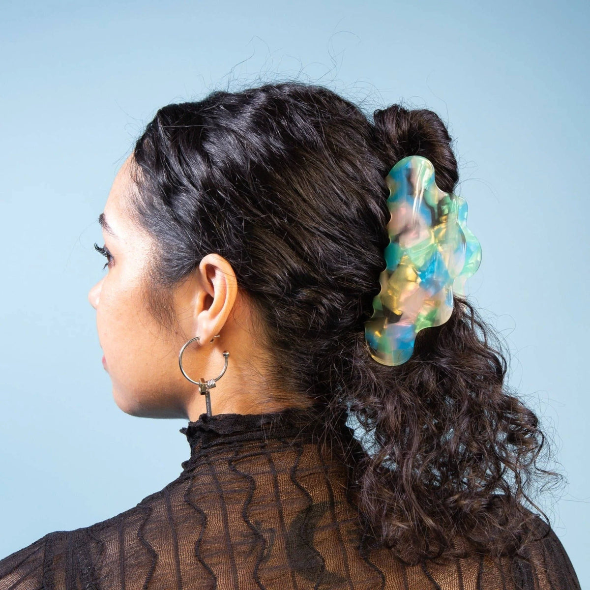 Translucent aqua-green jelly claw clip on dark hair bun, side view