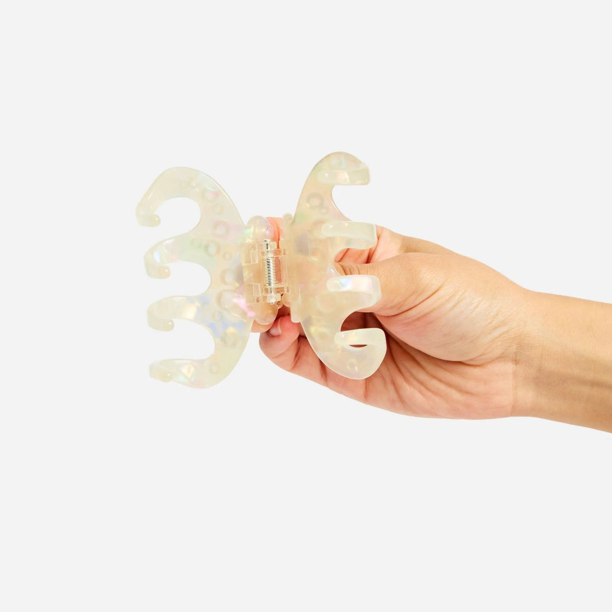 Octopus claw hair clip held open by hands, translucent pearl-shimmer cream.