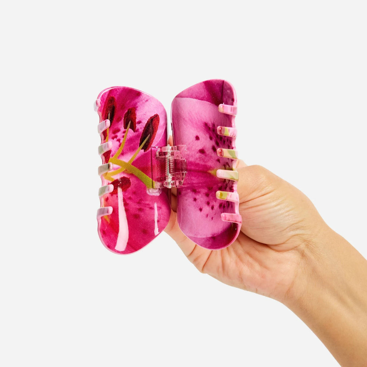 Pink lily-patterned claw hair clip held open, revealing gold-toned inner teeth