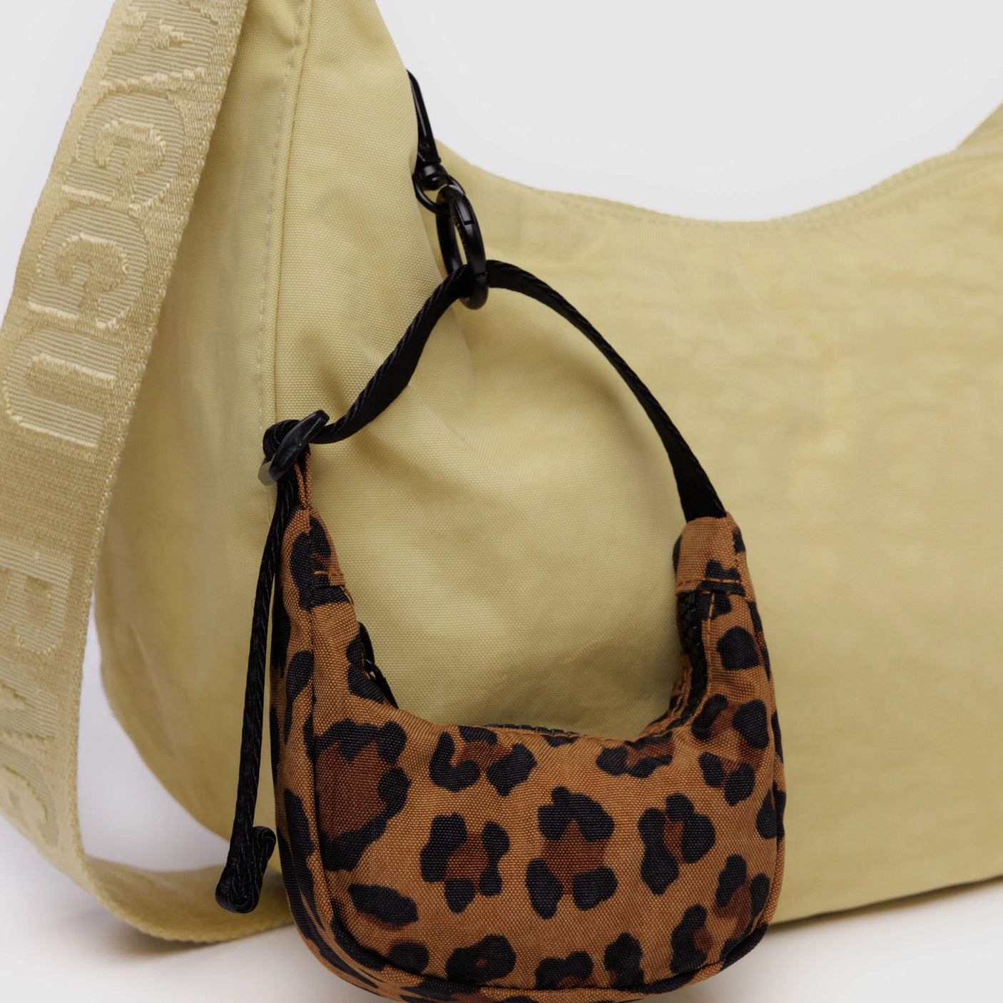 Leopard print mini bag attached to a larger beige shoulder bag with a logo strap.