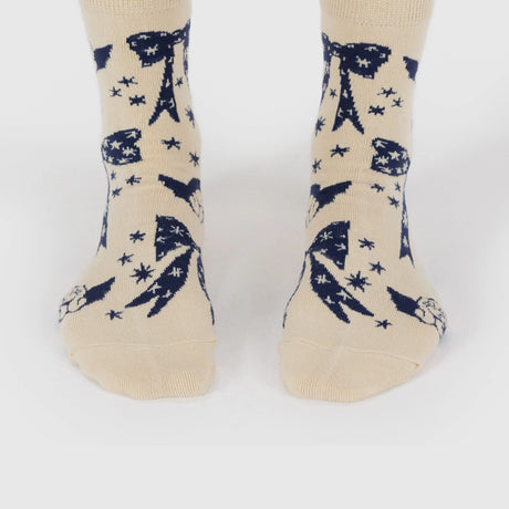 A pair of feet wear Baggu Crew Socks - Cherub Bows by Baggu, crafted from a bamboo rayon blend with a beige and blue bow, shooting star, and celestial pattern.