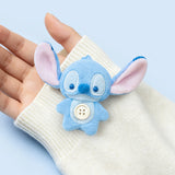 Blue Stitch-style plush charm with a round belly button, shown on a light knit cuff.