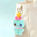 Teal plush character charm with pink flower topper and metal key ring on a tote.
