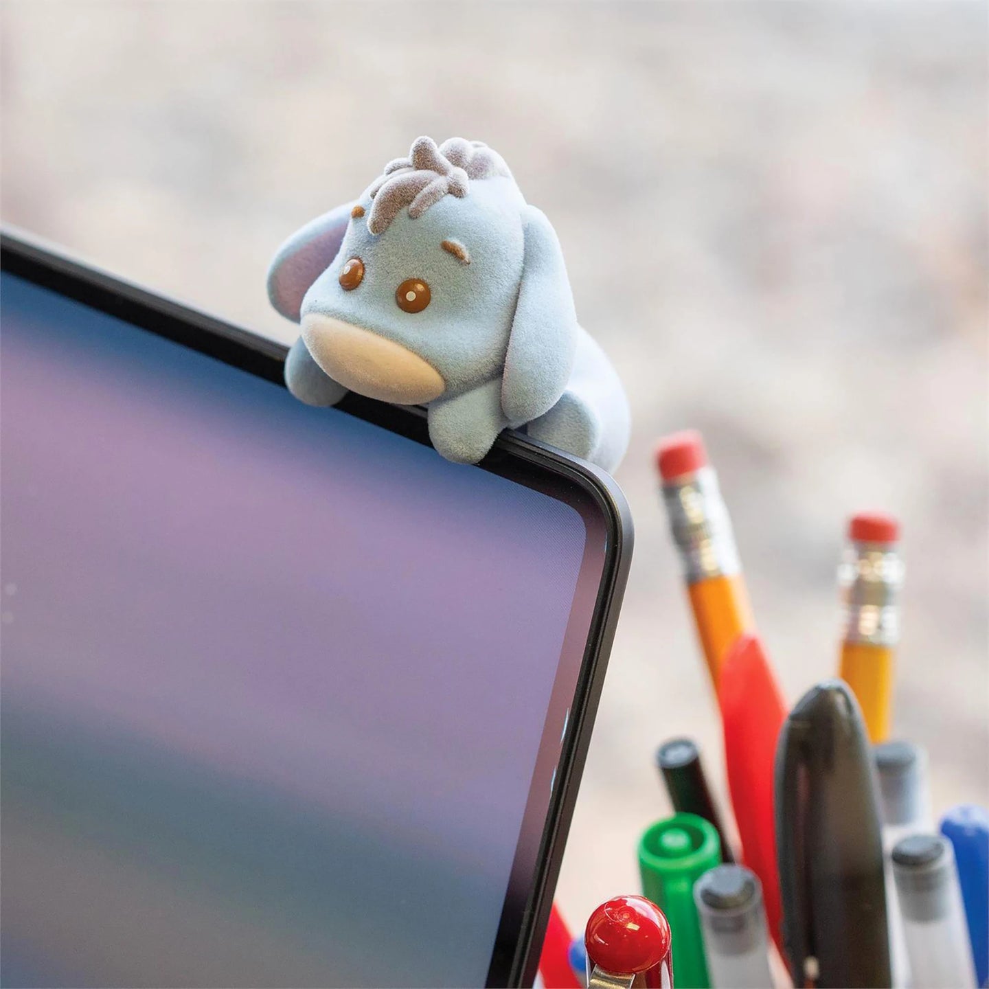 Light blue flocked plush climbing figure perched on a smartphone screen edge