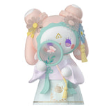 The Lucky EMMA - Secret Forest of Dim Lights Series Blind Box features a pastel-colored toy figure adorned with floral decorations and holding a magnifying glass. This delicate design, with soft pink and blue accents, beautifully captures the whimsical allure of a surprise from Lucky Emma's collection.