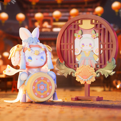 A whimsical rabbit toy in traditional attire stands beside a decorative round panel showcasing a design from the Lucky EMMA - Secret Forest of Dim Lights Series Blind Box. Lanterns hang out of focus in the background, adding an air of mystery similar to uncovering treasures within a Blind Box.