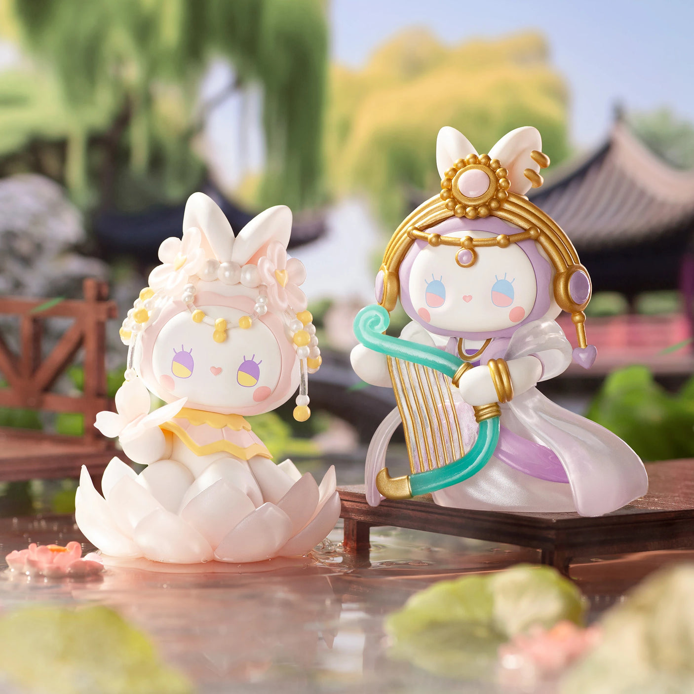 Two charming, rabbit-themed figurines from the Lucky EMMA - Secret Forest of Dim Lights Series Blind Box collection; one perched on a lotus flower and the other playing a harp, nestled in a tranquil Secret Forest scene featuring a pond and traditional architecture in the backdrop.