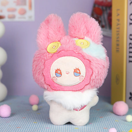 The Emma Fuzzy Family Keychain Blind Box by Lucky Emma features a plush toy with pink fur, yellow button eyes, and a white body—perfect as a cute keychain or bag charm for any collection. Pastel decorative background adds extra charm.