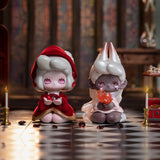 In the Lucky EMMA - Killa Treasure Pavilion Blind Box by Lucky Emma, two stylized figures stand on a checkered floor: one dressed in red, holding a jewel, and the other wearing a white robe and cradling a small flame. Flickering candles cast light against the wooden background, suggesting hidden treasures beyond what meets the eye.