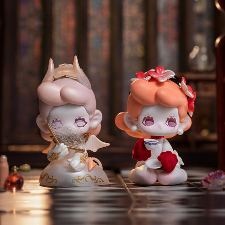 Two small figurines with pink hair; one, from the Killa Treasure Pavilion Blind Box by Lucky Emma, features horns and angel wings while holding a fan. The other figurine wears a floral headpiece and holds a teacup. Both have closed eyes and sit on a tiled surface, reminiscent of hidden gems from Secret Treasures.